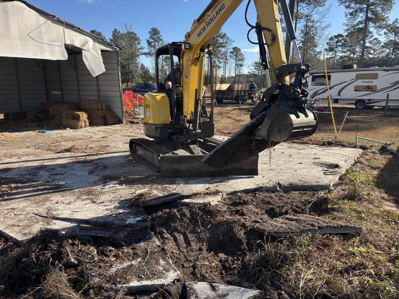 Excavator removing an old concrete pad on a job site